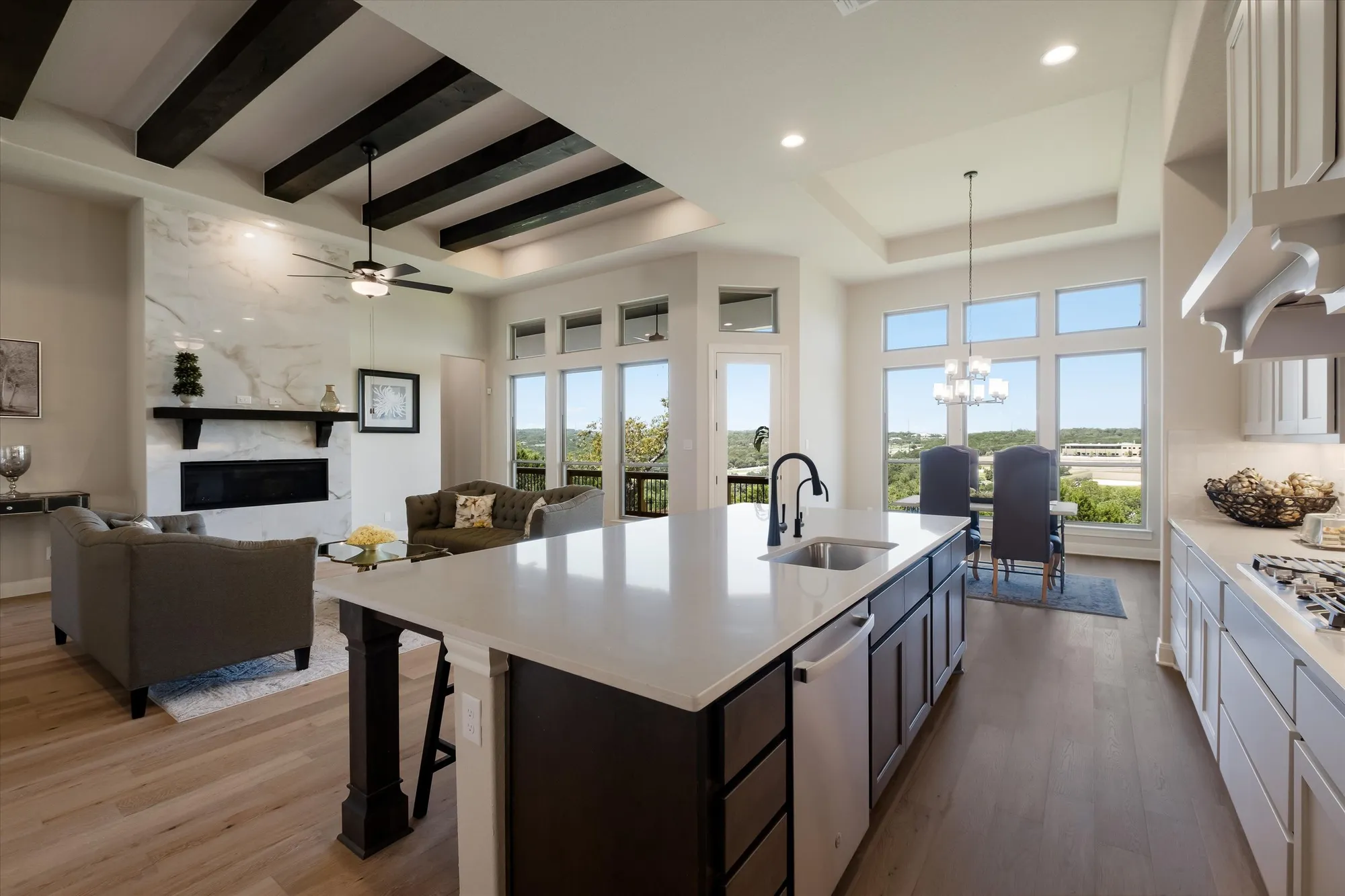 Open concept kitchen and living with dark island, exposed beams, and Hill Country views