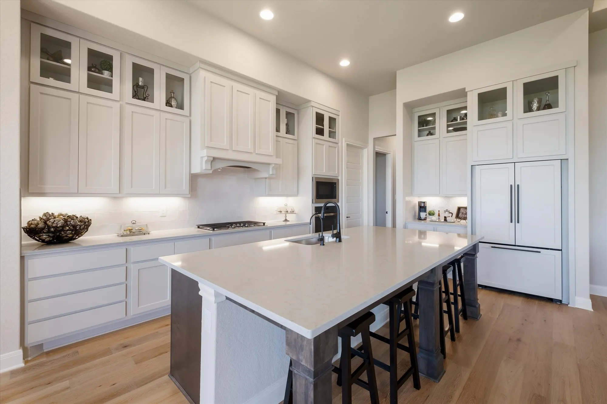 Kitchen with white shaker cabinets, dark island, and glass-front uppers