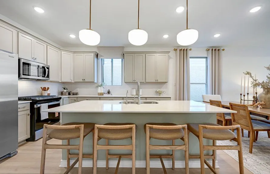 Sage-toned island kitchen with globe pendants and woven bar stools
